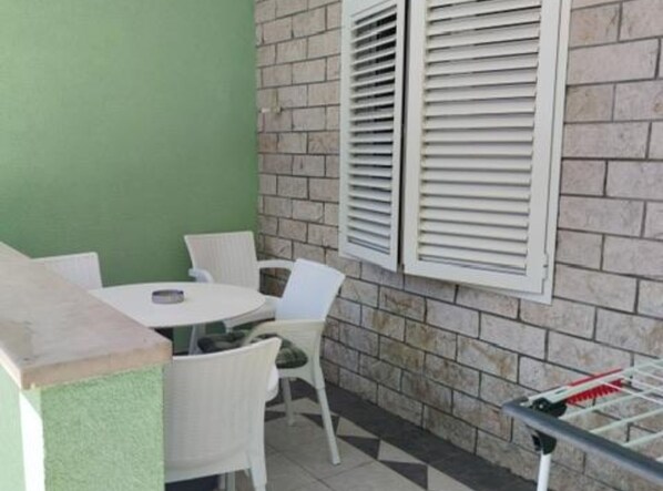 A small patio area with a round table and two white chairs, a brick wall, and a window with white shutters. - Apartments Villa Mira Roso (Makarska)
