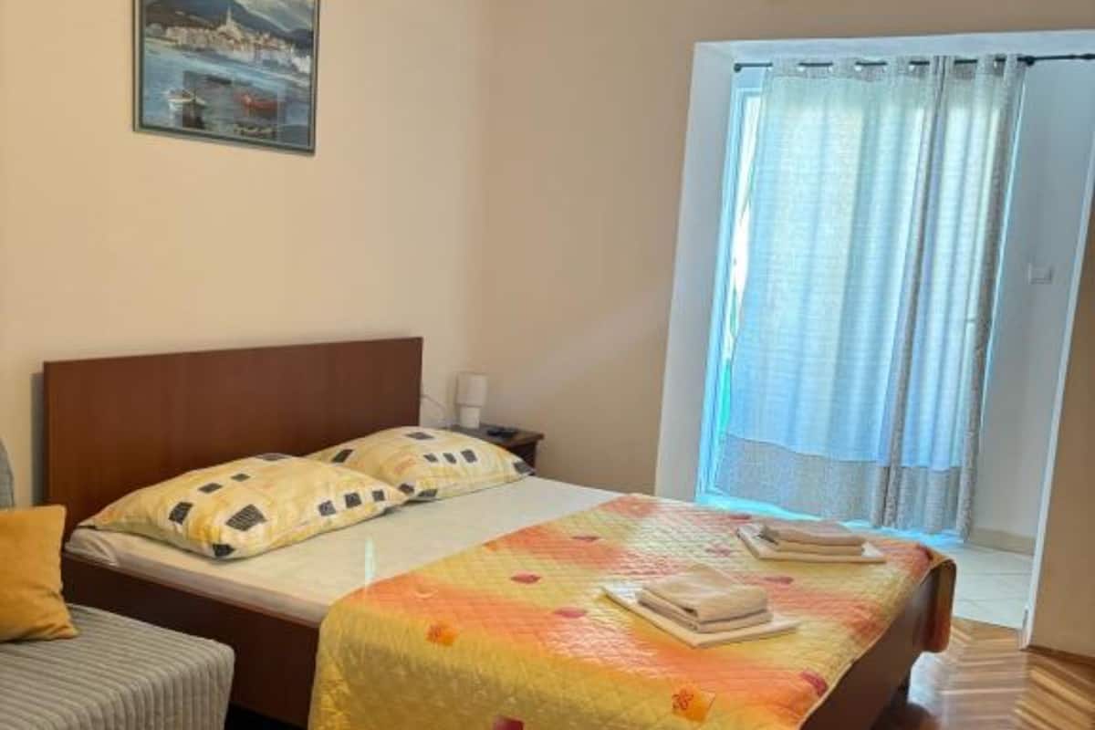 A hotel room with a bed, a nightstand, a lamp, a chair, and a window with curtains.