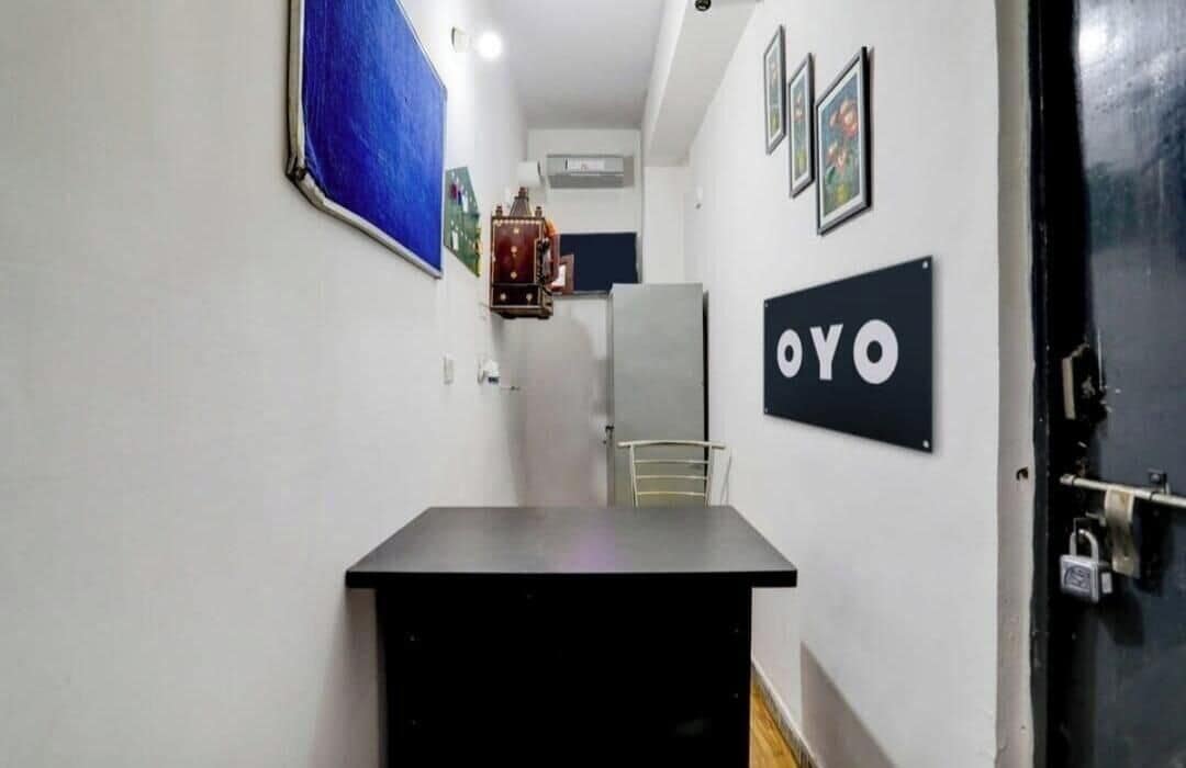 A narrow hallway with a black table, a refrigerator, and a door with a padlock.