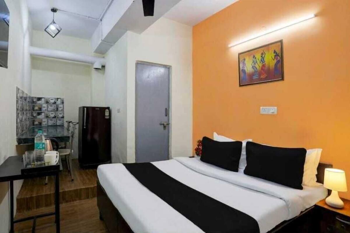 A hotel room with a bed, a desk, a refrigerator, and a door.