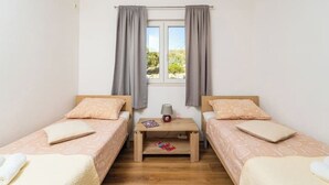 A room with two single beds, a small table with a lamp, and a window with curtains.