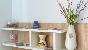A reception area with a white reception desk, a vase with flowers, a sign, and a small decorative item on the shelf.