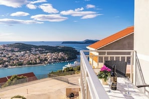 Un balcón con una mesa lista para dos personas, con vistas a un pueblo costero y un puerto.