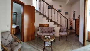 Ein Wohnzimmer mit Treppe, Korbmöbeln und Fliesenboden.