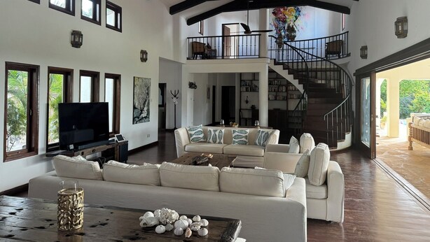 A spacious living room with a high ceiling, a large sofa, a coffee table with decorative items, and a television.