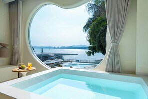 A large oval window in a room with a view of a pool and a body of water.