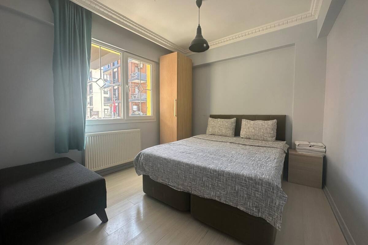 A bedroom with a bed, a bedside table, a window with curtains, and a radiator.