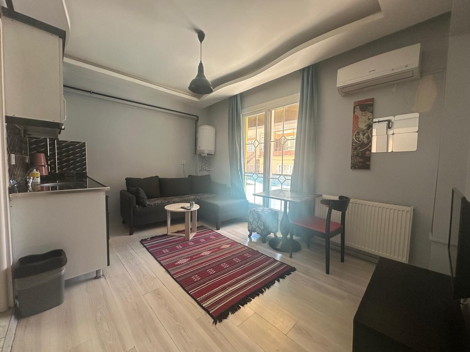 A modern living room with a sofa, a small round table, a red patterned rug, and a ceiling fan.