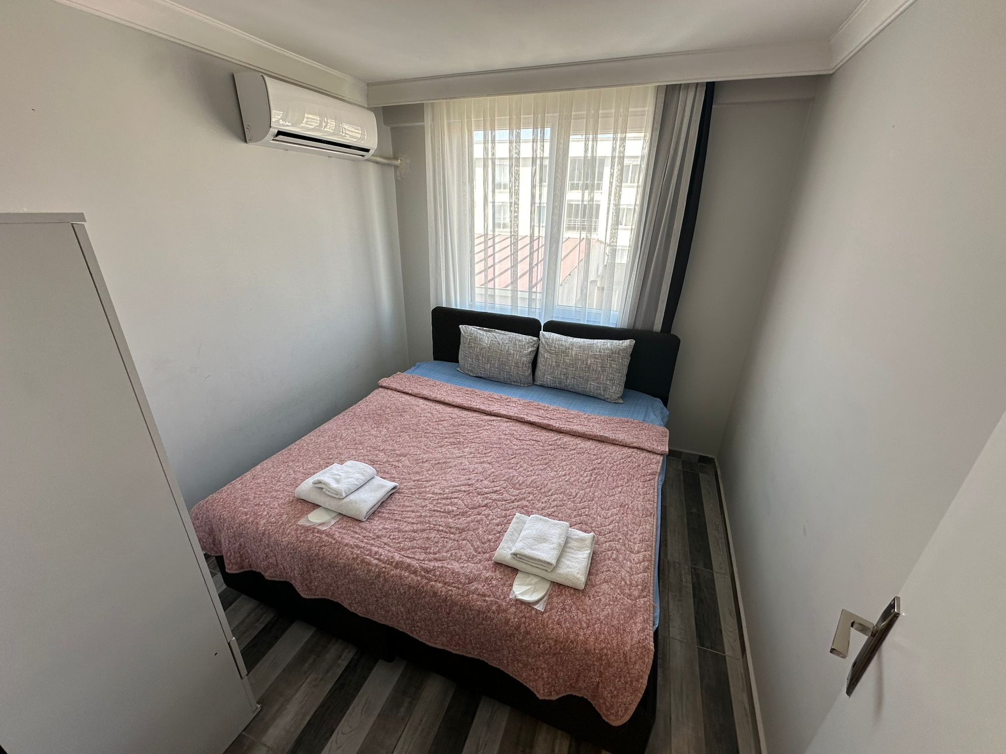 A small, neatly arranged bedroom with a bed, pillows, and a pink blanket.