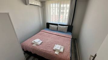 A small, neatly arranged bedroom with a bed, pillows, and a pink blanket.