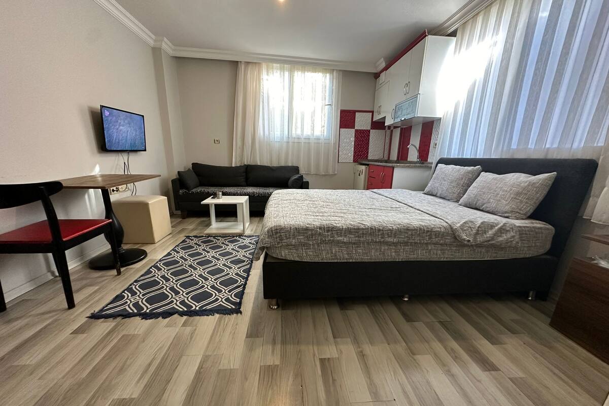 A hotel room with a bed, a small table, a sofa, a TV, and a kitchenette.
