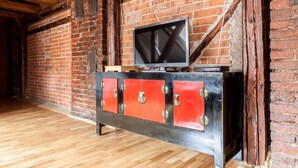 A room with a brick wall, wooden beams, a television on a red and black cabinet, and a wooden floor.