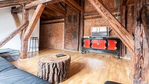 A loft-style room with exposed wooden beams, a brick wall, a wooden floor, a red cabinet, and a television.
