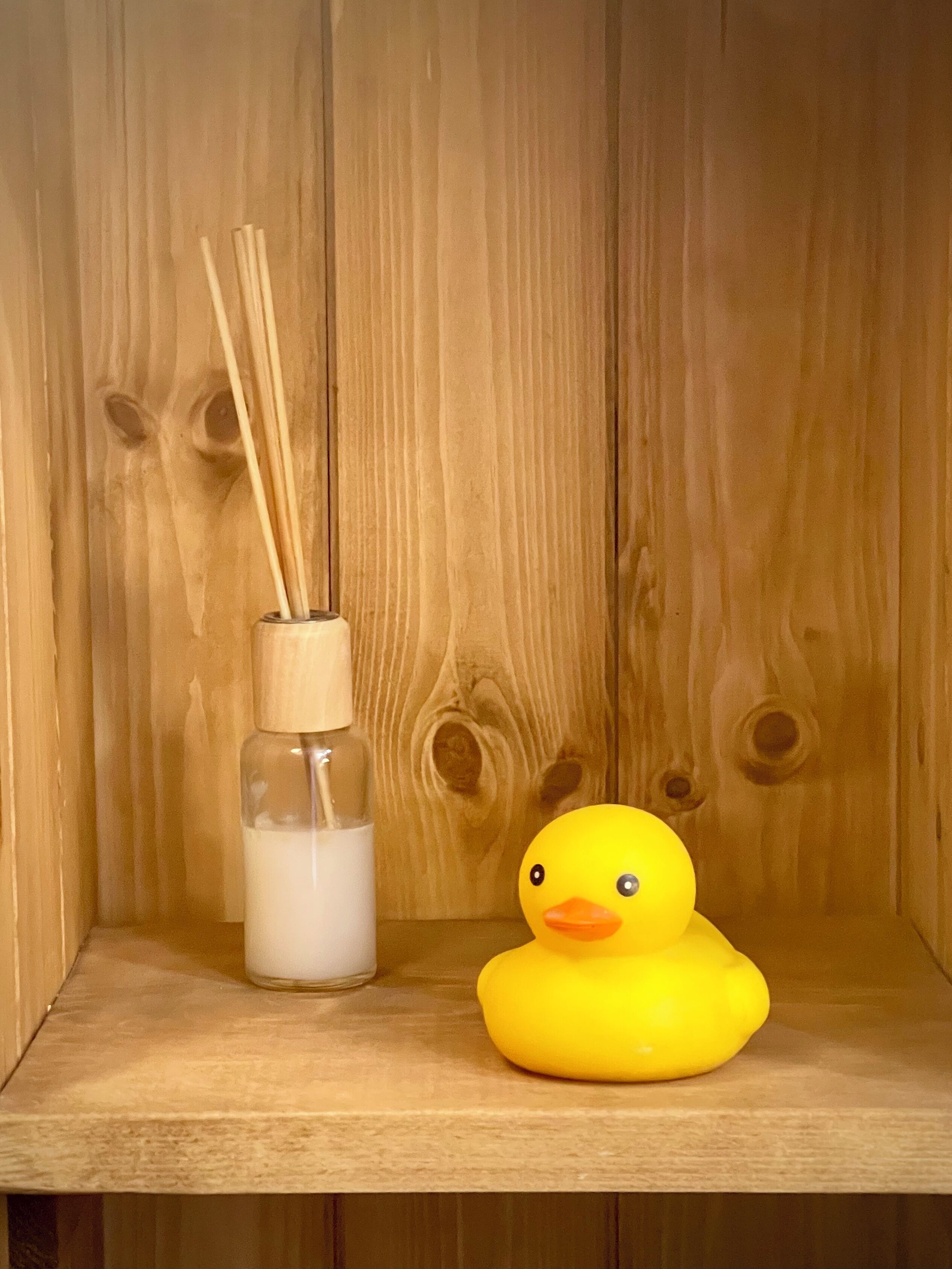 Una repisa de madera con una botella de vidrio y un patito de goma.