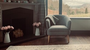 A room with a fireplace, a window with a view of the outdoors, a chair, and a vase with flowers. - Chic retreat with a beautiful sea view (Milford)