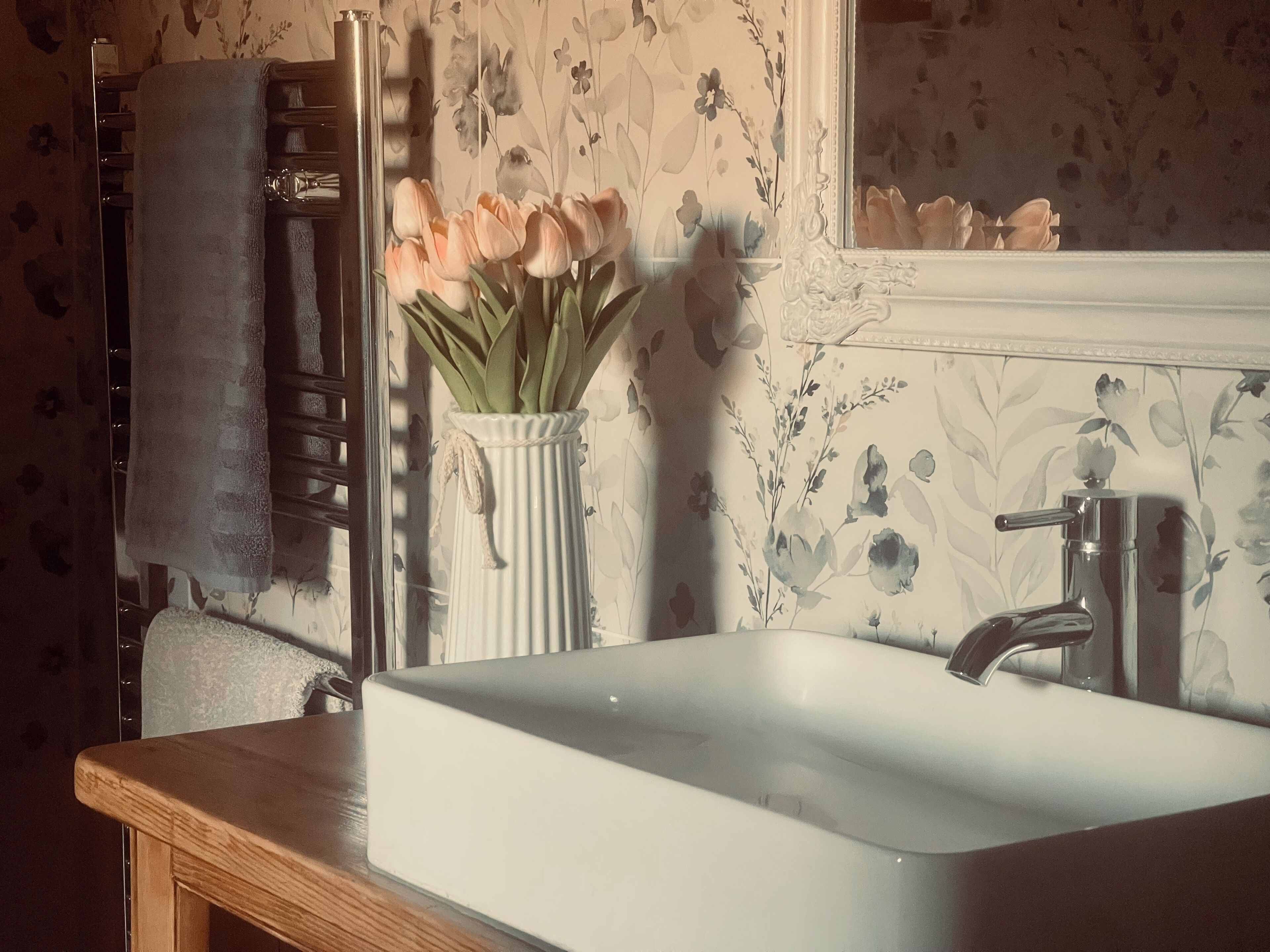 A bathroom with a white sink, a mirror, and a vase of flowers.