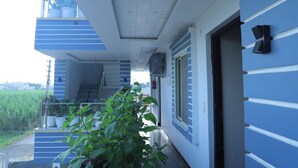 Un bâtiment moderne à la façade bleue et blanche, doté d’un escalier apparent et d’un balcon agrémenté de plantes en pot.