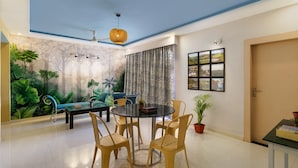 A dining area with a round table, four chairs, a sofa, and a potted plant. - Lazy Daze By Unique Choice Hotels (Udaipur)