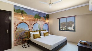 A bedroom with a bed, a nightstand, a ceiling fan, a window with a view, and a decorative wall mural. - Lazy Daze By Unique Choice Hotels (Udaipur)