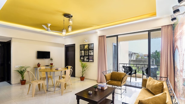 A modern living room with a dining area, a sofa, and a balcony with a view. - Lazy Daze By Unique Choice Hotels (Udaipur)