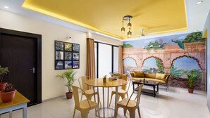 A modern living room with a round dining table, comfortable seating, and a mural on the wall. - Lazy Daze By Unique Choice Hotels (Udaipur)