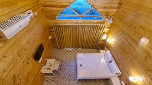 A small, wooden cabin with a bed, a table, a chair, a window, and a wall-mounted heater. - Aranya Abode (Arambol)