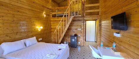 A wooden cabin with a bed, desk, and a small refrigerator.