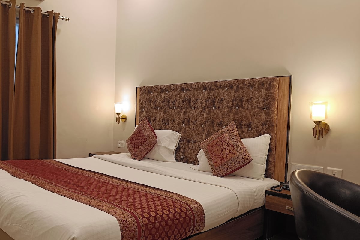 Une chambre d’hôtel avec un grand lit, deux lampes de chevet, une tête de lit à motifs et une couvre-lit rouge et blanche.