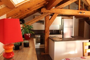 Una cocina con vigas de madera, una lámpara roja, plantas en macetas y un refrigerador.