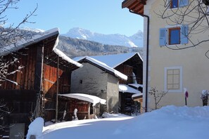 Un edificio tradicional de madera con tejado cubierto de nieve, pared de piedra y montañas al fondo.