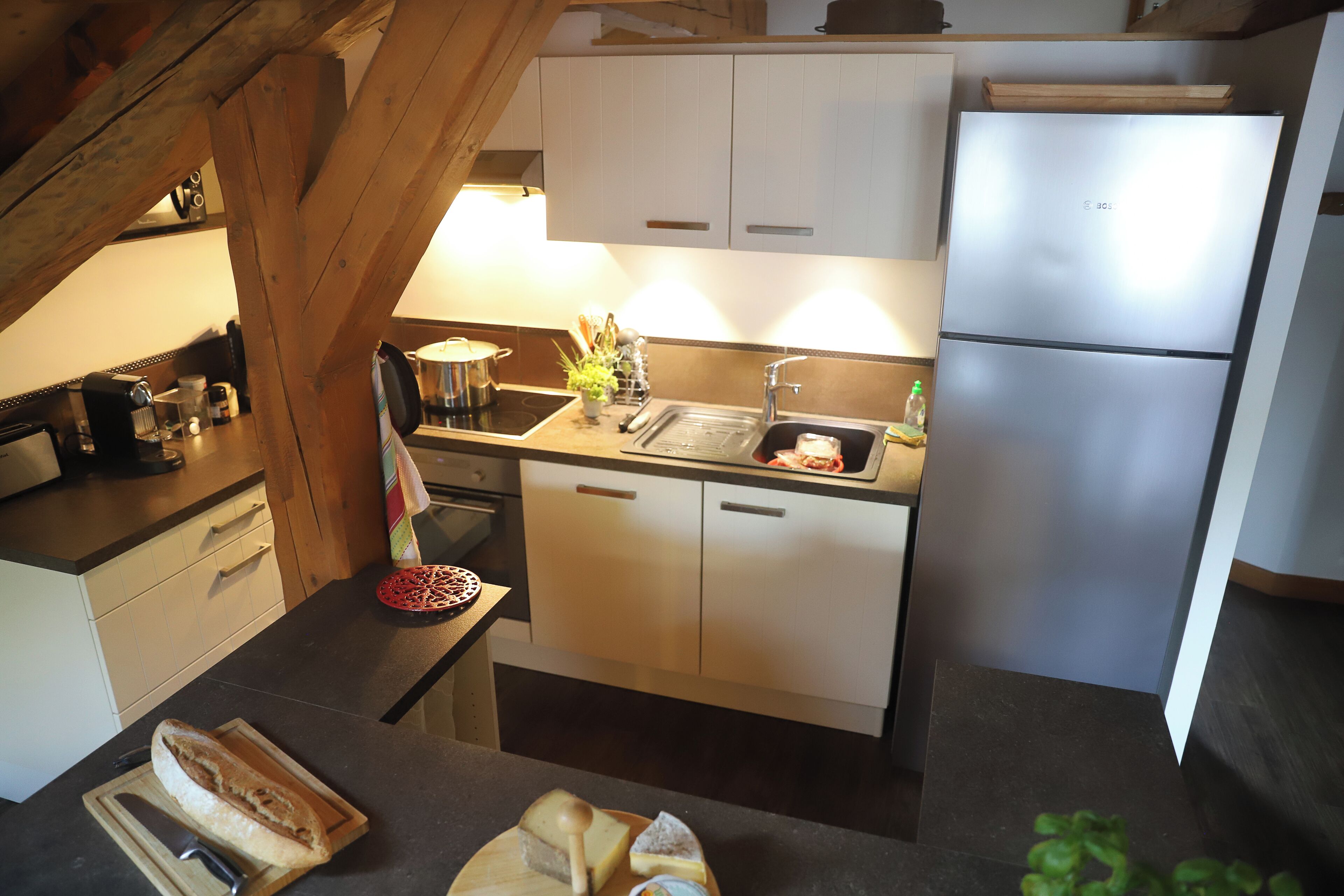 A compact kitchen with white cabinets, a stainless steel refrigerator, and a wooden countertop.