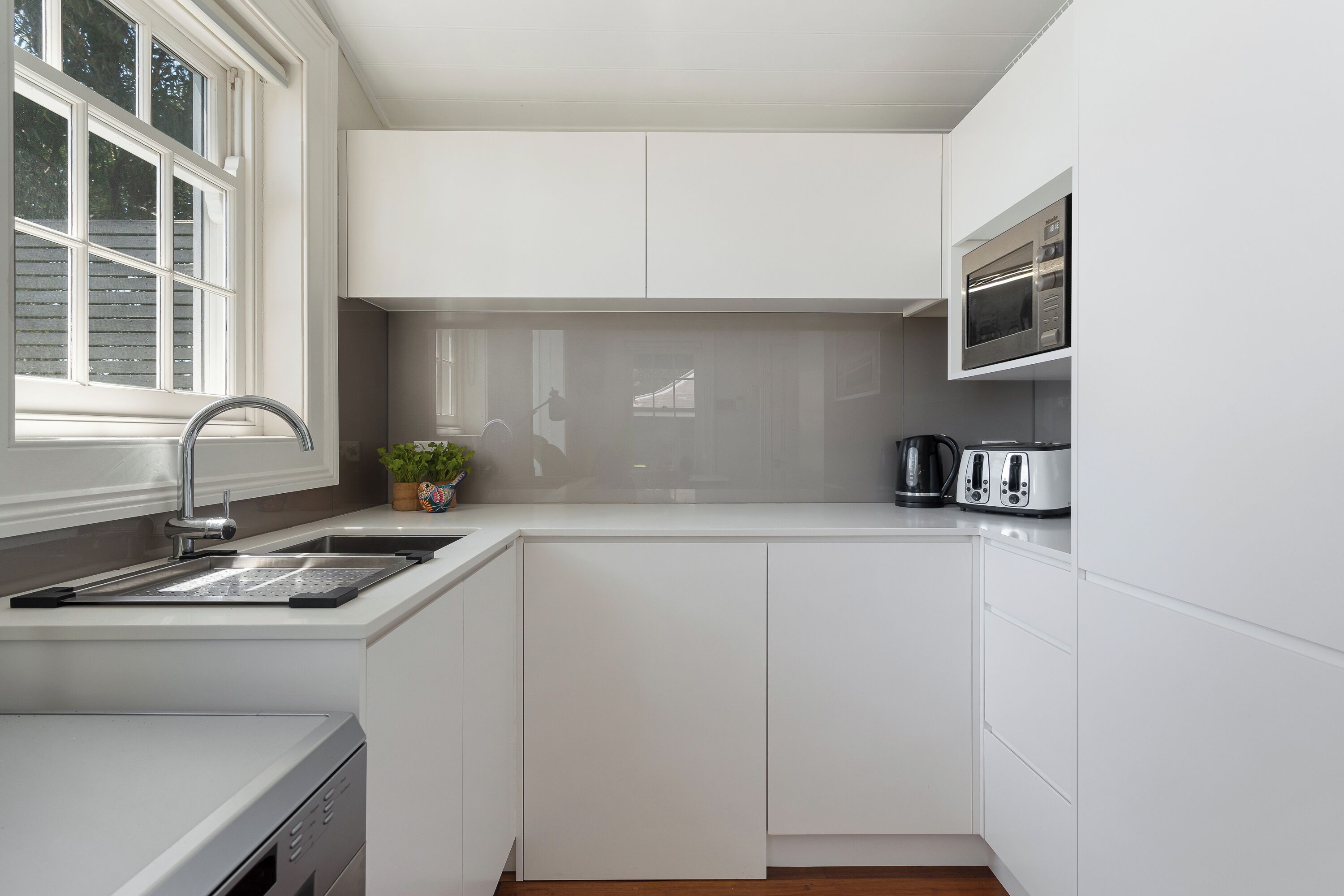 Une cuisine moderne avec des meubles blancs, un évier en acier inoxydable, un four à micro-ondes et un grille-pain.