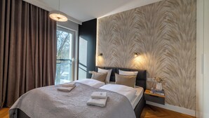 A modern hotel room with a large bed, a nightstand with a vase, and a patterned wall.