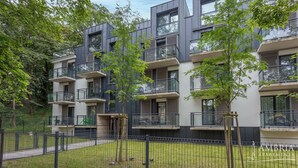 A modern apartment building with multiple balconies, large windows, and a fenced courtyard.