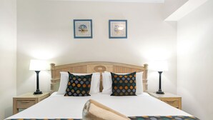 A neatly made bed with a polka dot bedspread, two matching pillows, and a wooden headboard. There are two bedside tables with lamps, and two framed pictures on the wall above the bed.