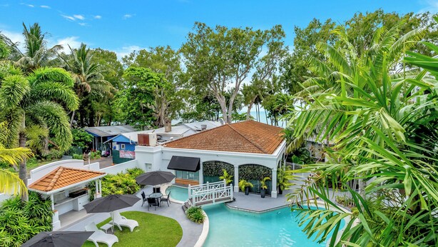 Ett semesterparadis med en swimmingpool, solstolar, parasoller och frodig grönska.