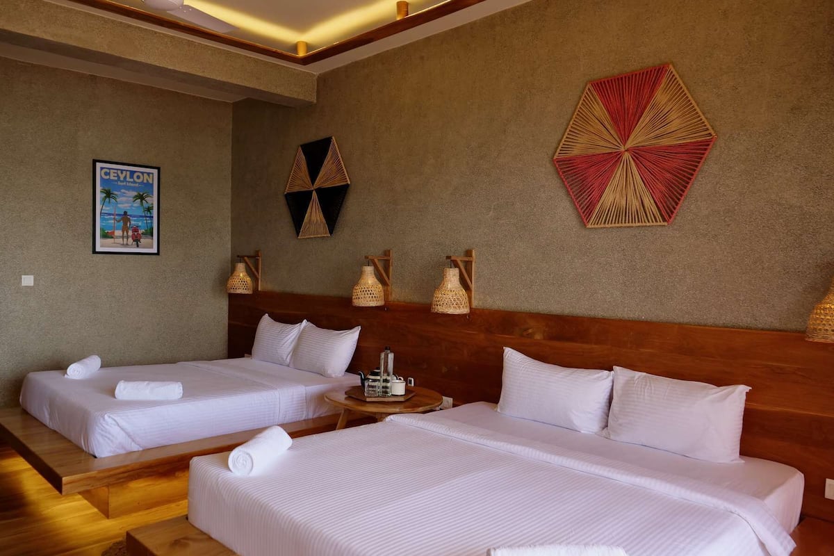 A hotel room with two beds, a wooden headboard, a small table with a lamp, and wall art.