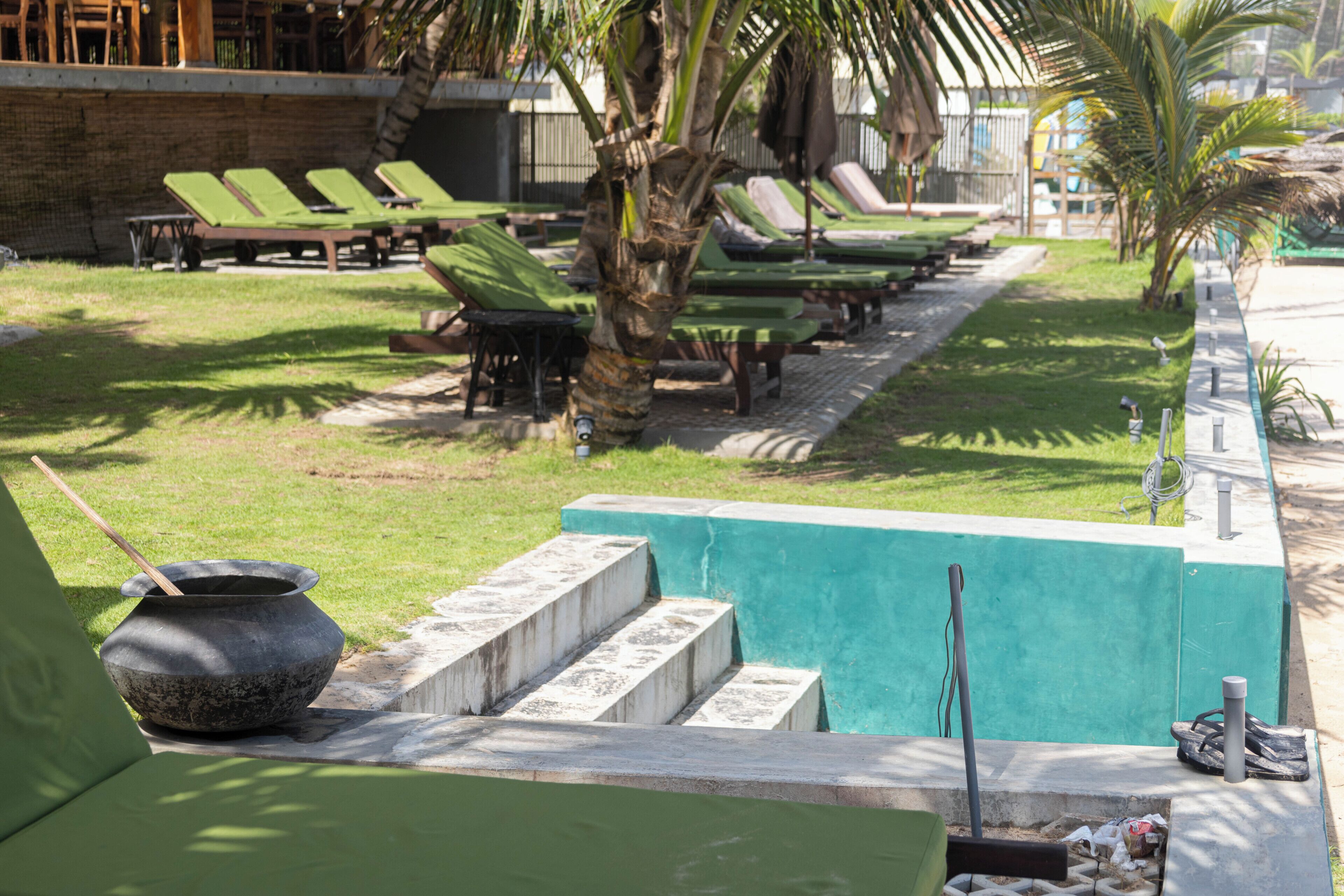 Uma área à beira da piscina com espreguiçadeiras, uma bacia de pedra e degraus que dão acesso à piscina.