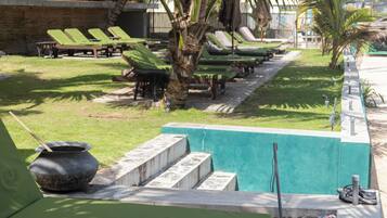 Uma área à beira da piscina com espreguiçadeiras, uma bacia de pedra e degraus que dão acesso à piscina.
