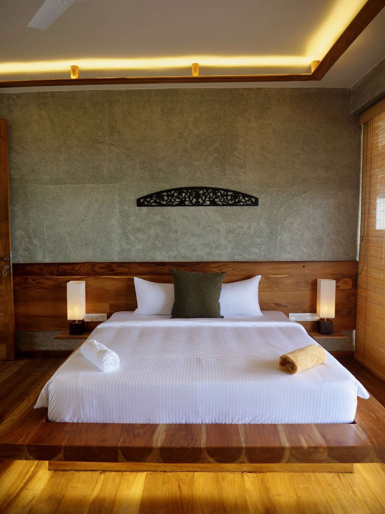 A neatly made bed with white linens, two bedside lamps, and a decorative wall piece above it.