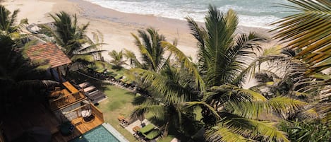 A resort with a swimming pool, beach view, and palm trees.