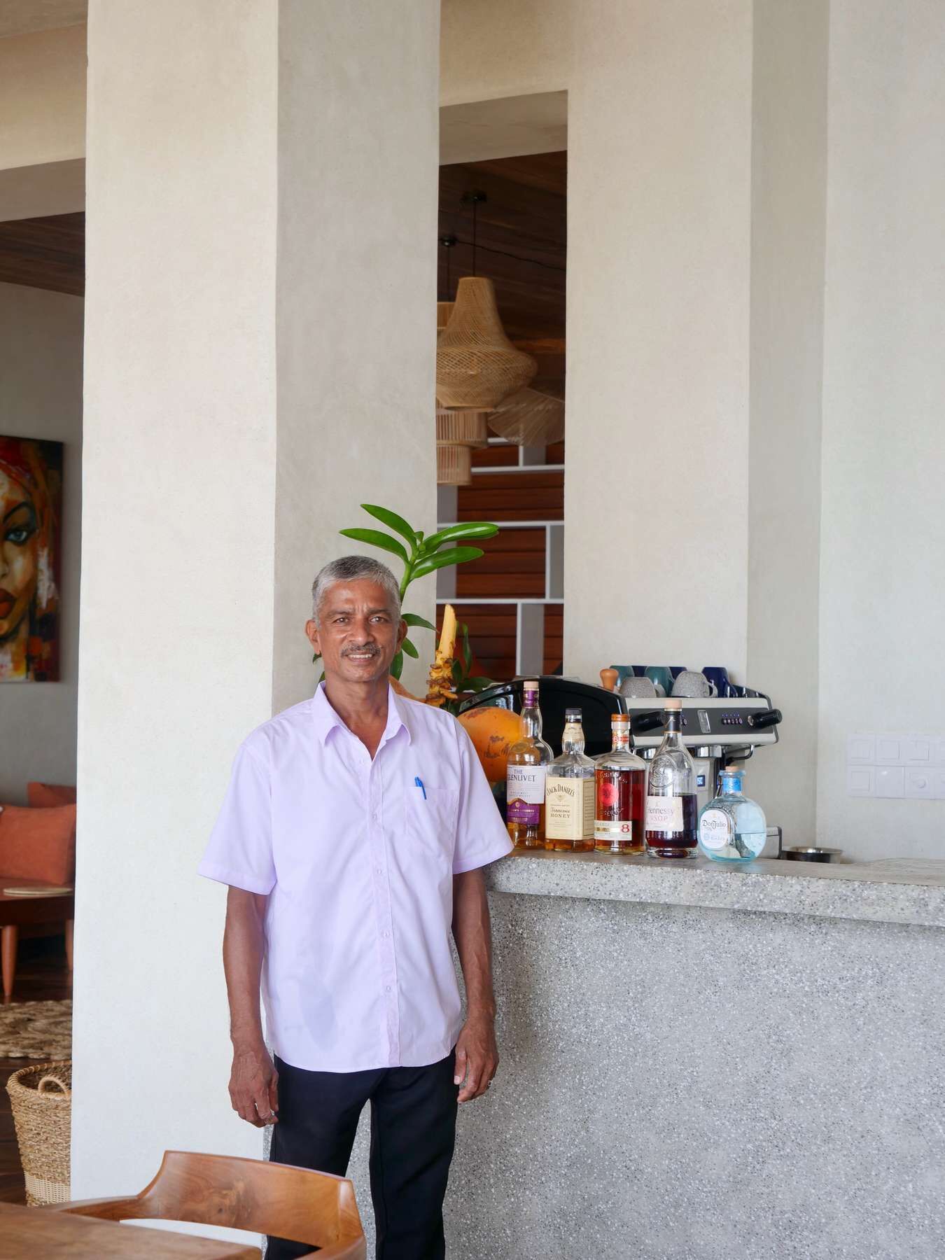 A man standing in a room with a bar area featuring various bottles and a coffee machine.