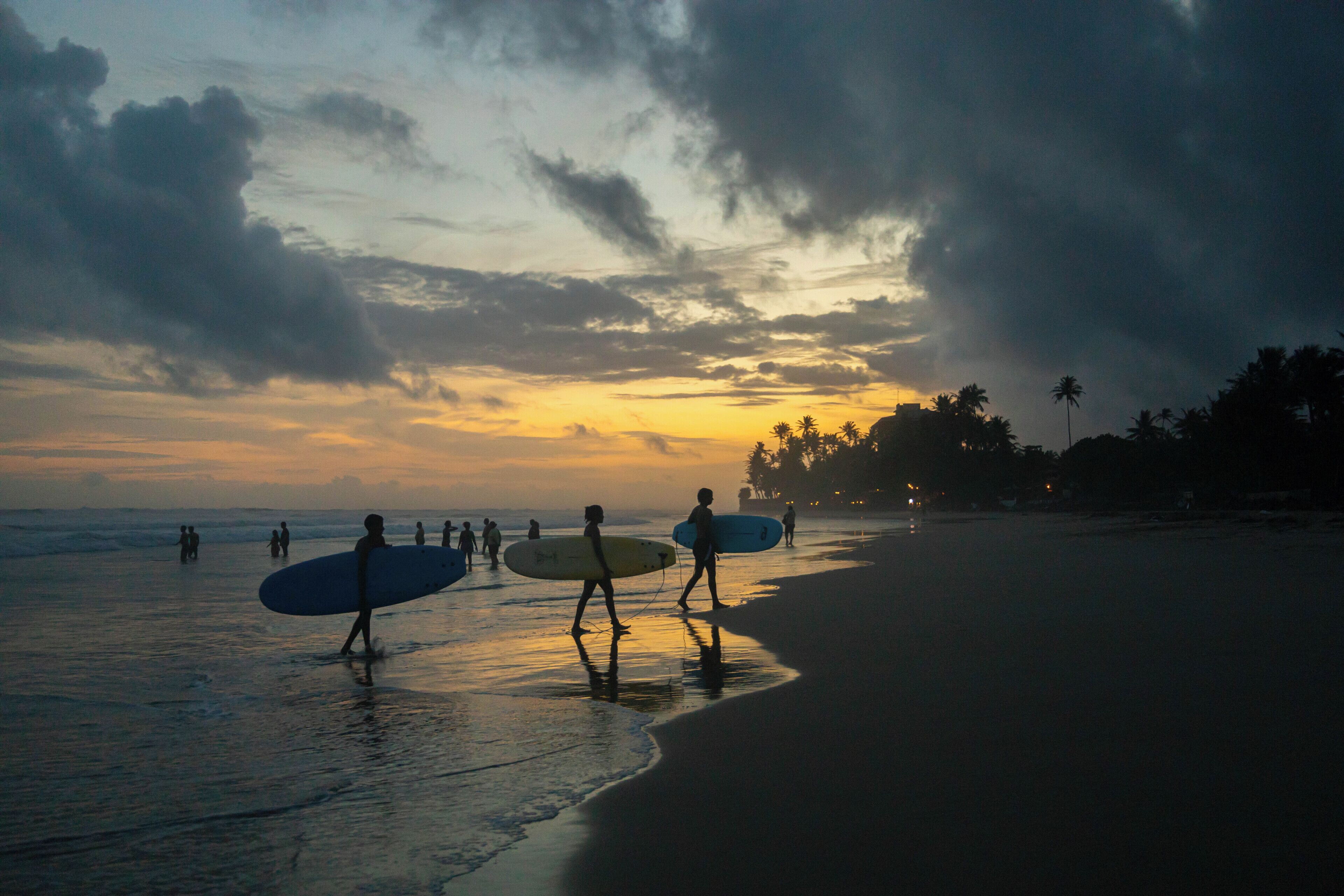 A beach scene with people walking along the shore, some carrying surfboards.