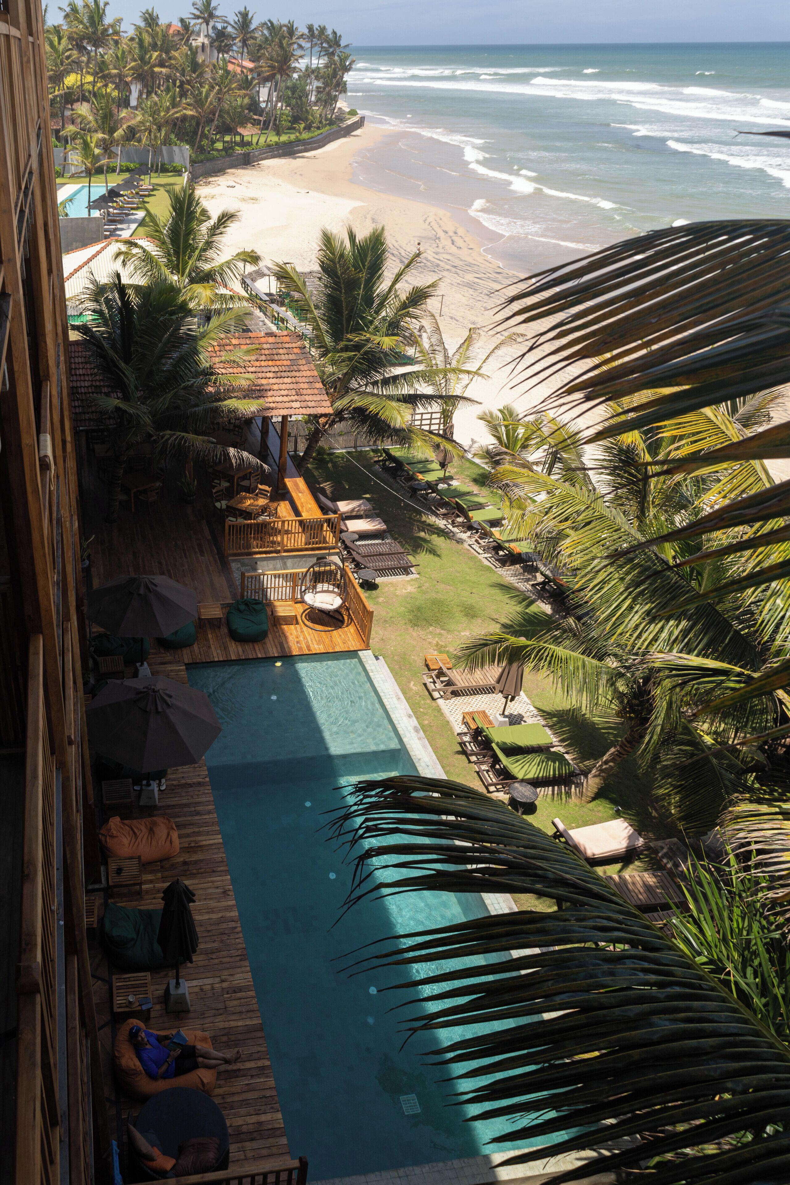 A pool area with lounge chairs and umbrellas, overlooking a beach and ocean.