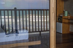 A wooden deck with a view of the ocean, a small kitchenette, and a seating area with cushions.