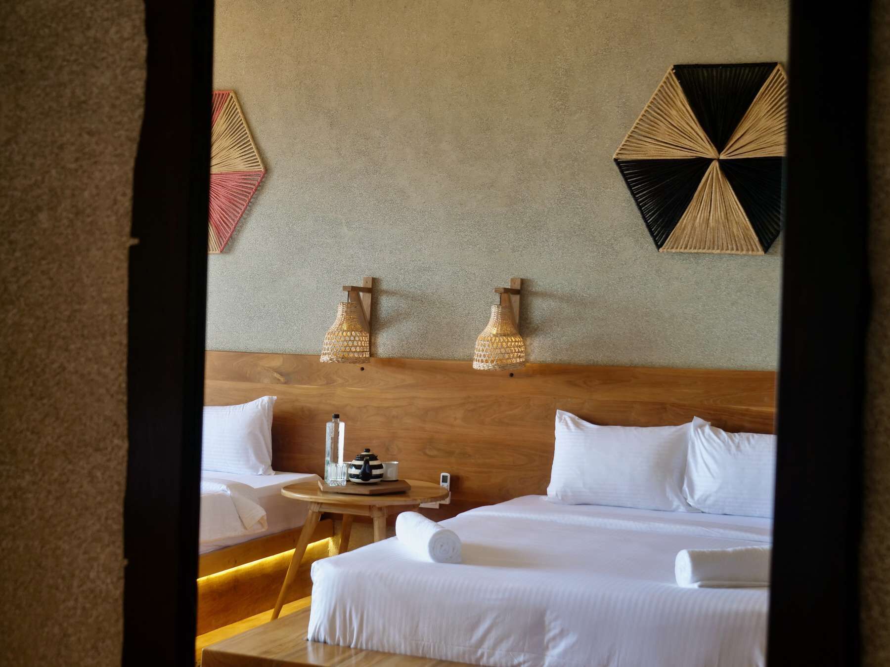 A hotel room with two beds, a wooden headboard, a small round table with a lamp, and decorative wall art.