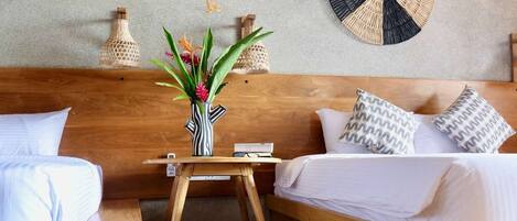 A modern bedroom with a wooden headboard, a round woven wall decoration, a small wooden table with a vase of flowers, and a blue throw blanket.