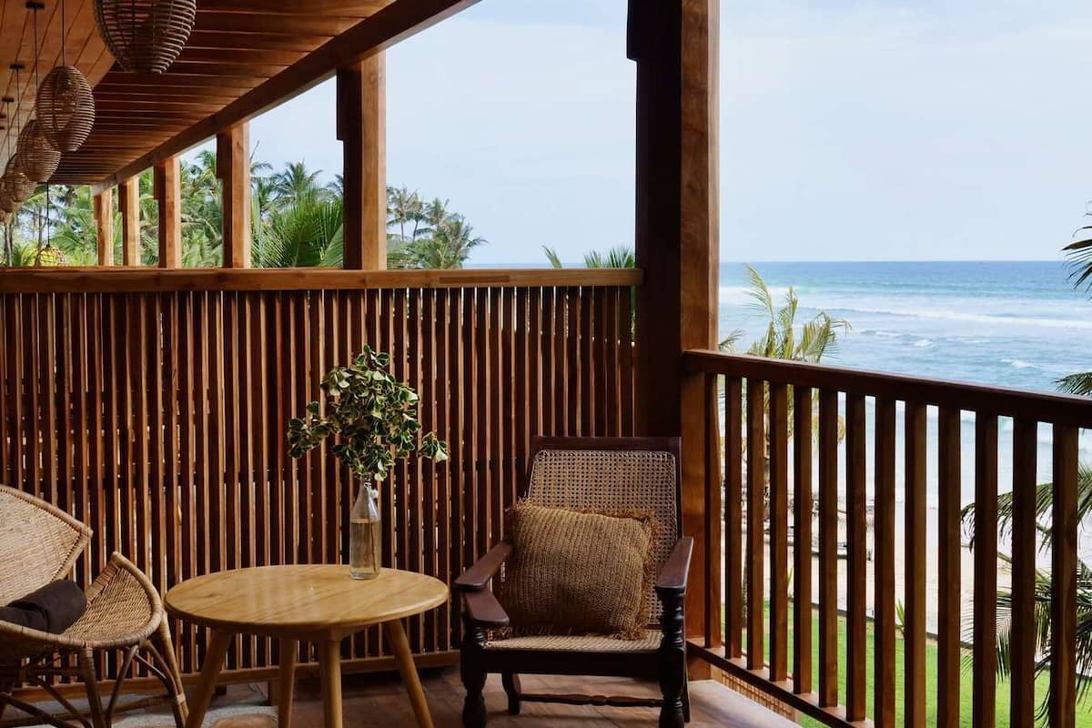 A wooden deck with a view of the ocean, featuring wicker chairs, a round table, and a hanging light fixture.