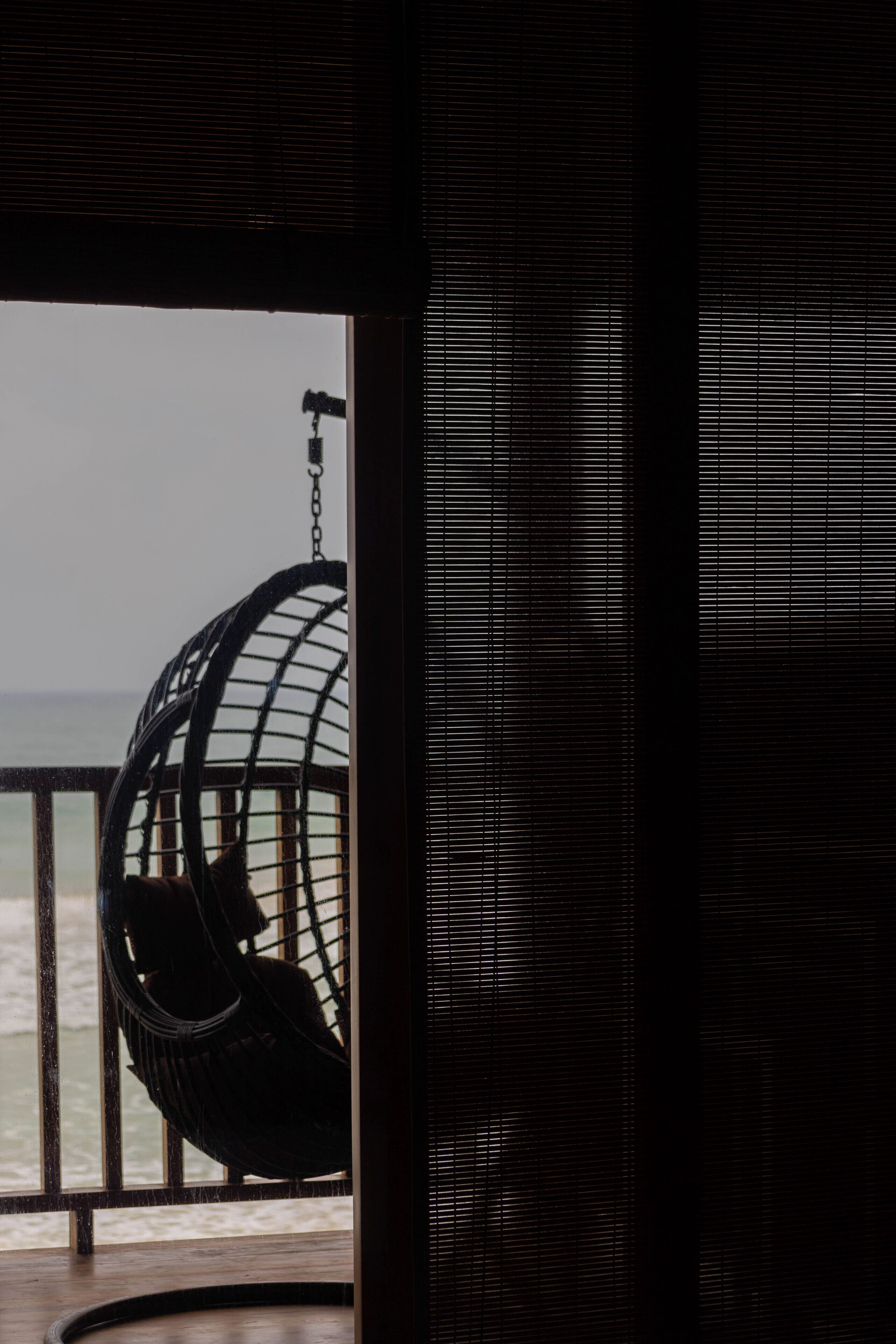 Una habitación con vista al mar, una silla colgante y una ventana con persianas.