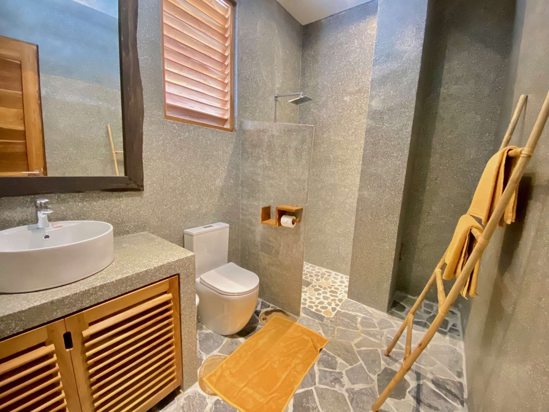 A bathroom with a stone floor, a white sink, a toilet, and a shower.
